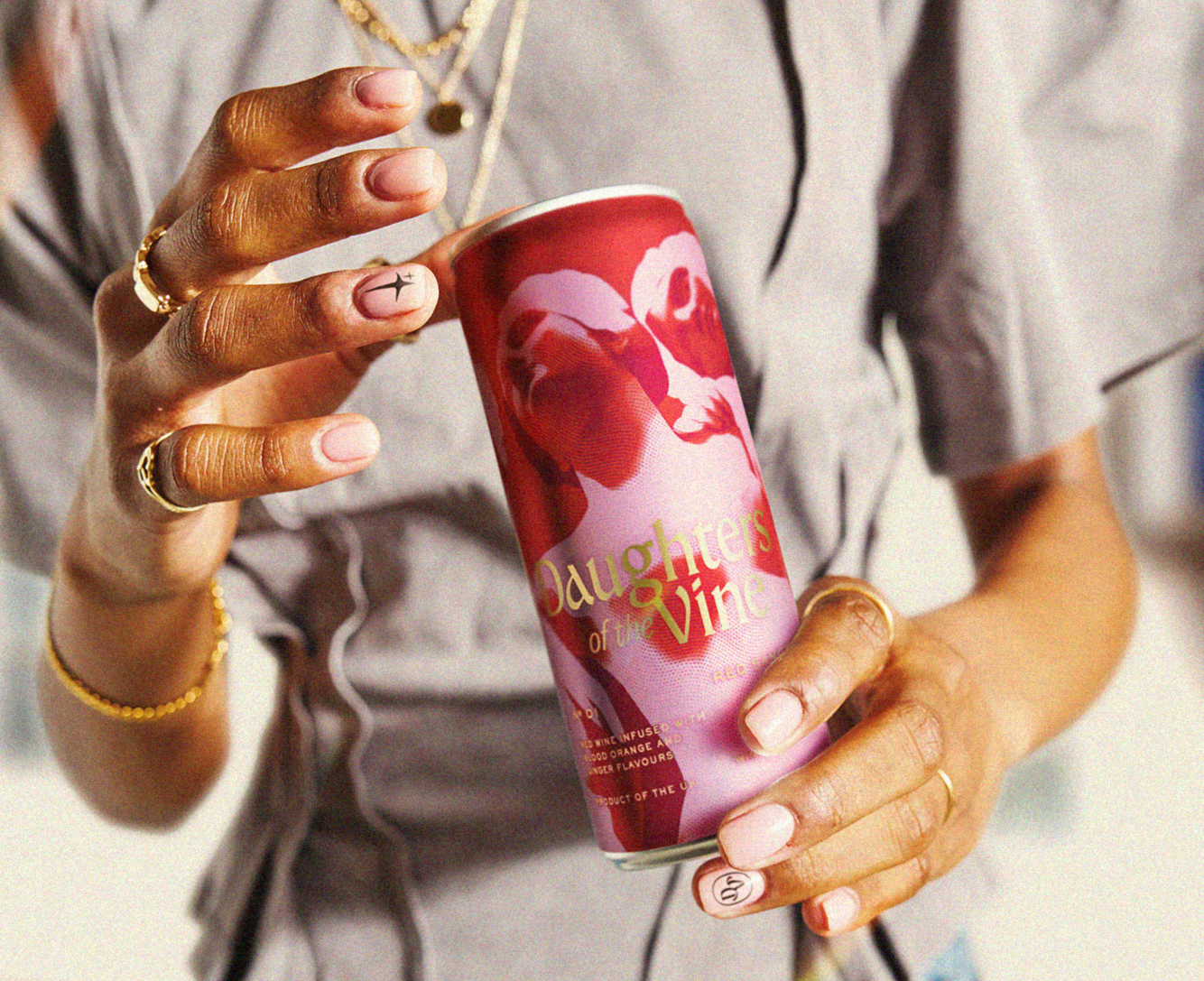 Person holding Daughters of the Vine red sangria can with artistic red and pink design featuring faces